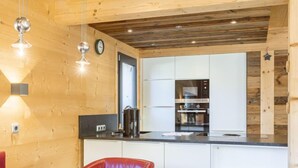 Eine moderne Küche mit Holzwänden, einem Edelstahlbackofen und einer Essecke mit roten Stühlen.