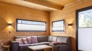 Ein gemütliches Blockhaussinnere mit einer Couch, einem kleinen Tisch und zwei Fenstern mit Jalousien.