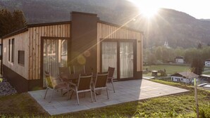 A modern wooden house with a patio, large windows, and a view of the mountains.