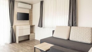 A modern, well-lit living room with a grey sofa, a small wooden table, and a flat-screen TV mounted on the wall. - mit 2 Schlafzimmern by Interhome (Kötschach-Mauthen)