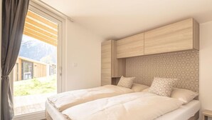 Un dormitorio con cama, cabecera, mesita de noche y vistas al exterior.