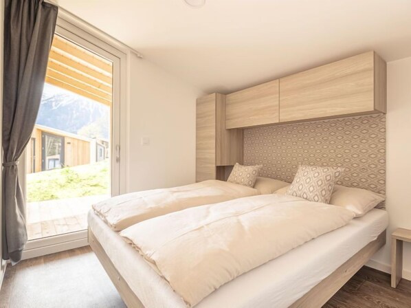 A bedroom with a bed, a headboard, a nightstand, and a view of the outdoors. - Premium mit 2 Schlafzimmern by Interhome (Kötschach-Mauthen)