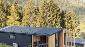 Una cabaña moderna con techo plano, ventanas grandes y una terraza.