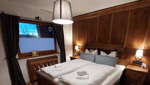 A wooden four-poster bed with white linens and towels, two bedside tables with lamps, a window with curtains, and a wooden wall paneling. - BIBERCHALET and BIBERBAU as compl. House with terrace, garden and garden sauna (Bad Lauterberg im Harz)