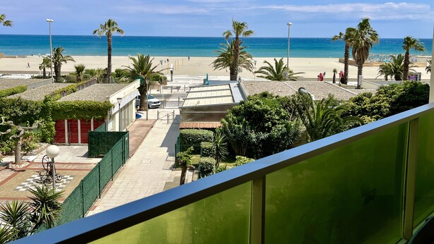 Vista de una playa con palmeras, cielo despejado y un edificio con techo de tejas al frente.
