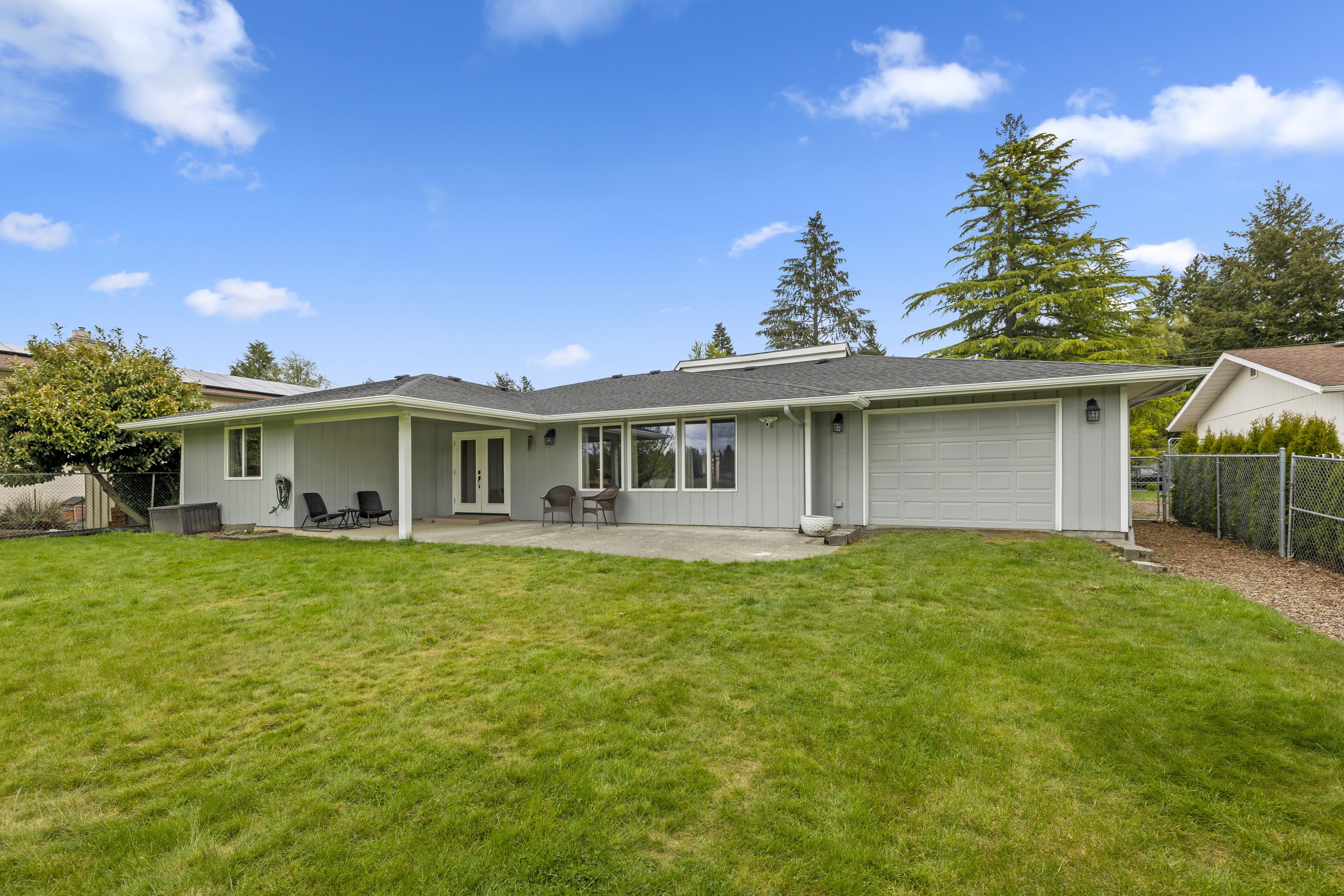 Ein Bungalow mit überdachter Terrasse, Garage und gepflegtem Rasen.
