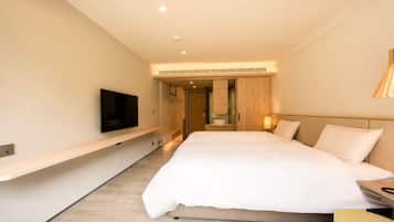 A modern hotel room with a large bed, a mounted TV, a bedside table, and a built-in bench along the wall.