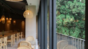 Un comedor moderno con sillas de mimbre y una larga mesa de madera, ventanas amplias con vistas a abundante follaje.