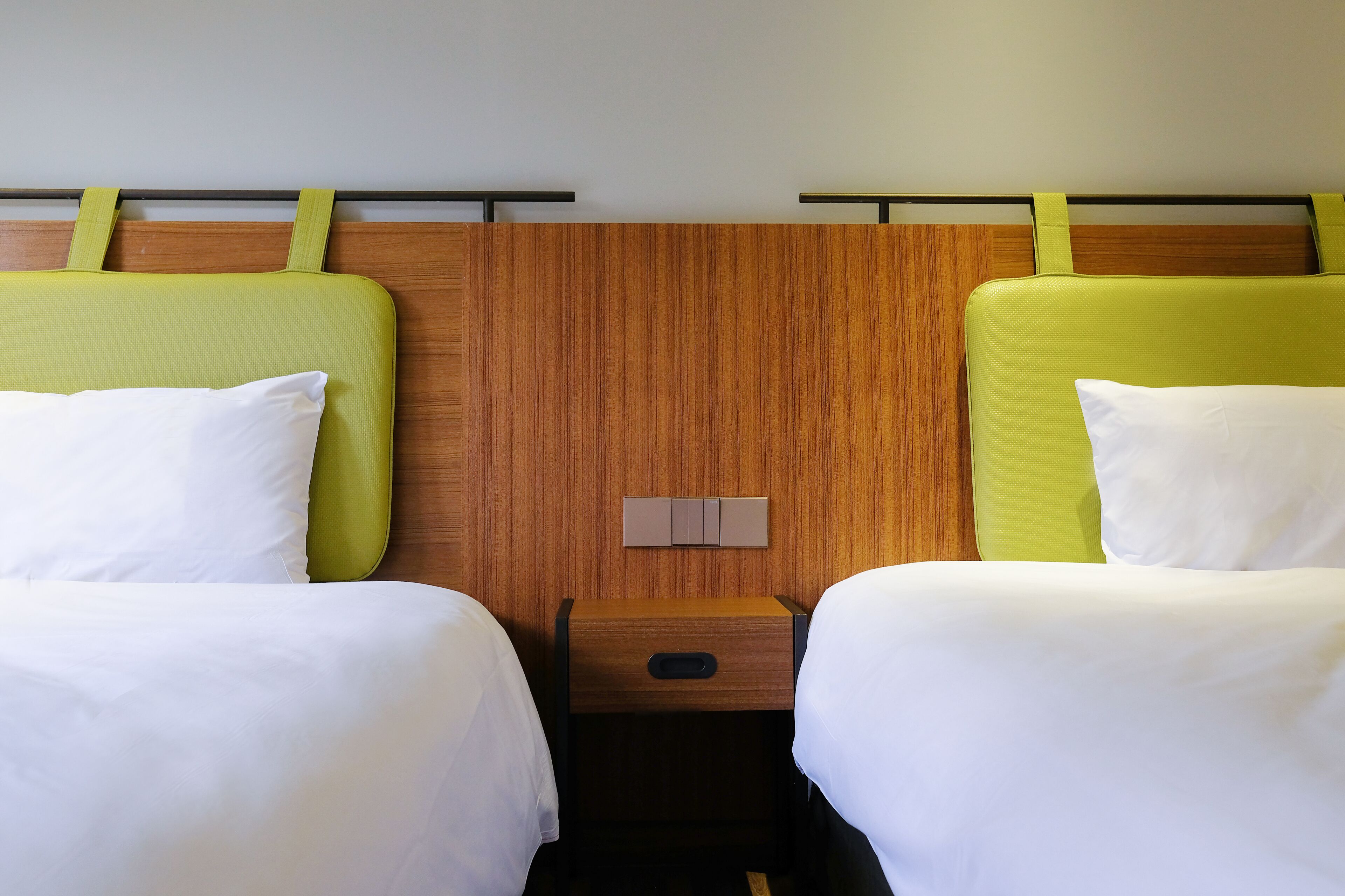 Quarto de hotel com duas camas, cada uma com cabeceira verde e roupa de cama branca.