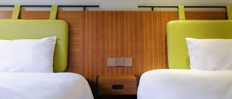 Quarto de hotel com duas camas, cada uma com cabeceira verde e roupa de cama branca.