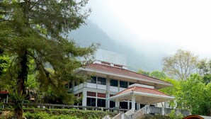 Un edificio de varios pisos con tejado de tejas rojas, rodeado de exuberante vegetación y un paisaje montañoso.
