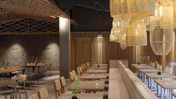 A modern dining area with long tables and chairs, wooden paneling, and hanging light fixtures.