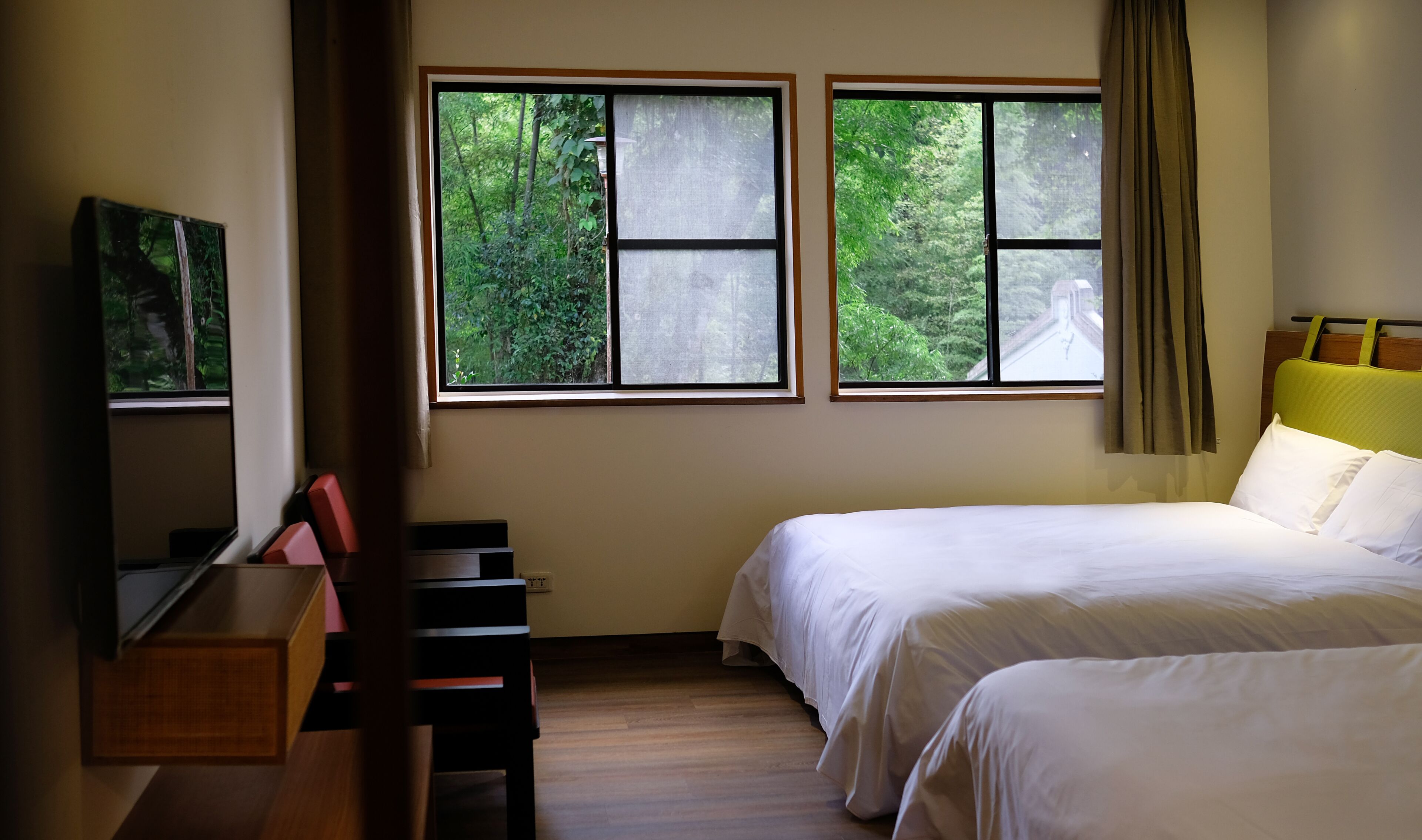 Quarto de hotel com duas camas, uma televisão e janelas amplas com cortinas.