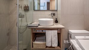 Un baño moderno con ducha envuelta en vidrio, un lavabo redondo y un espejo sobre él.