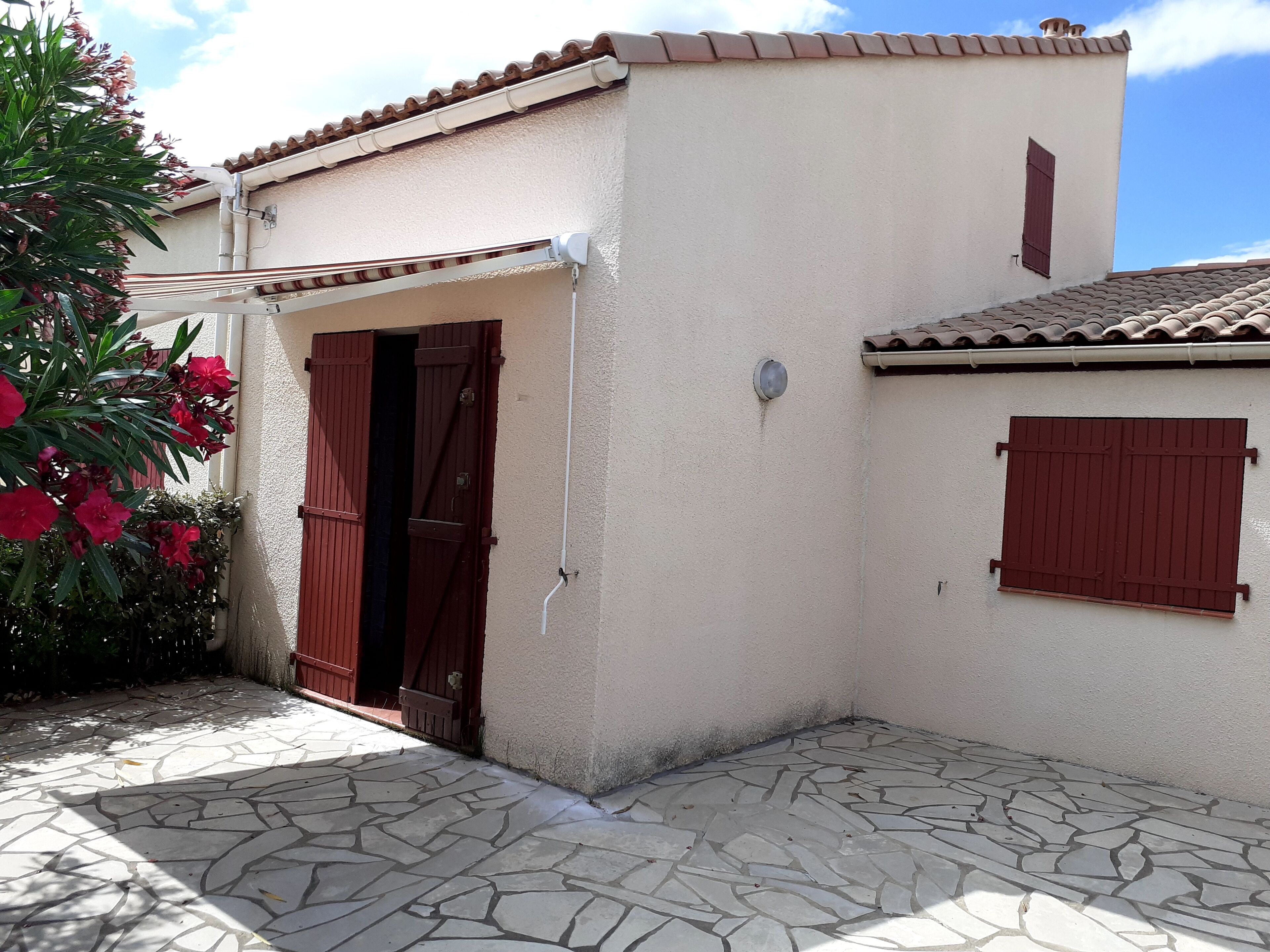 A building with a tiled roof, a stone-paved entrance, and a door with a shutter.