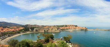 Une ville côtière dotée d’imposantes fortifications, d’un port où sont amarrés des bateaux et d’où l’on a une vue dégagée sur la mer.