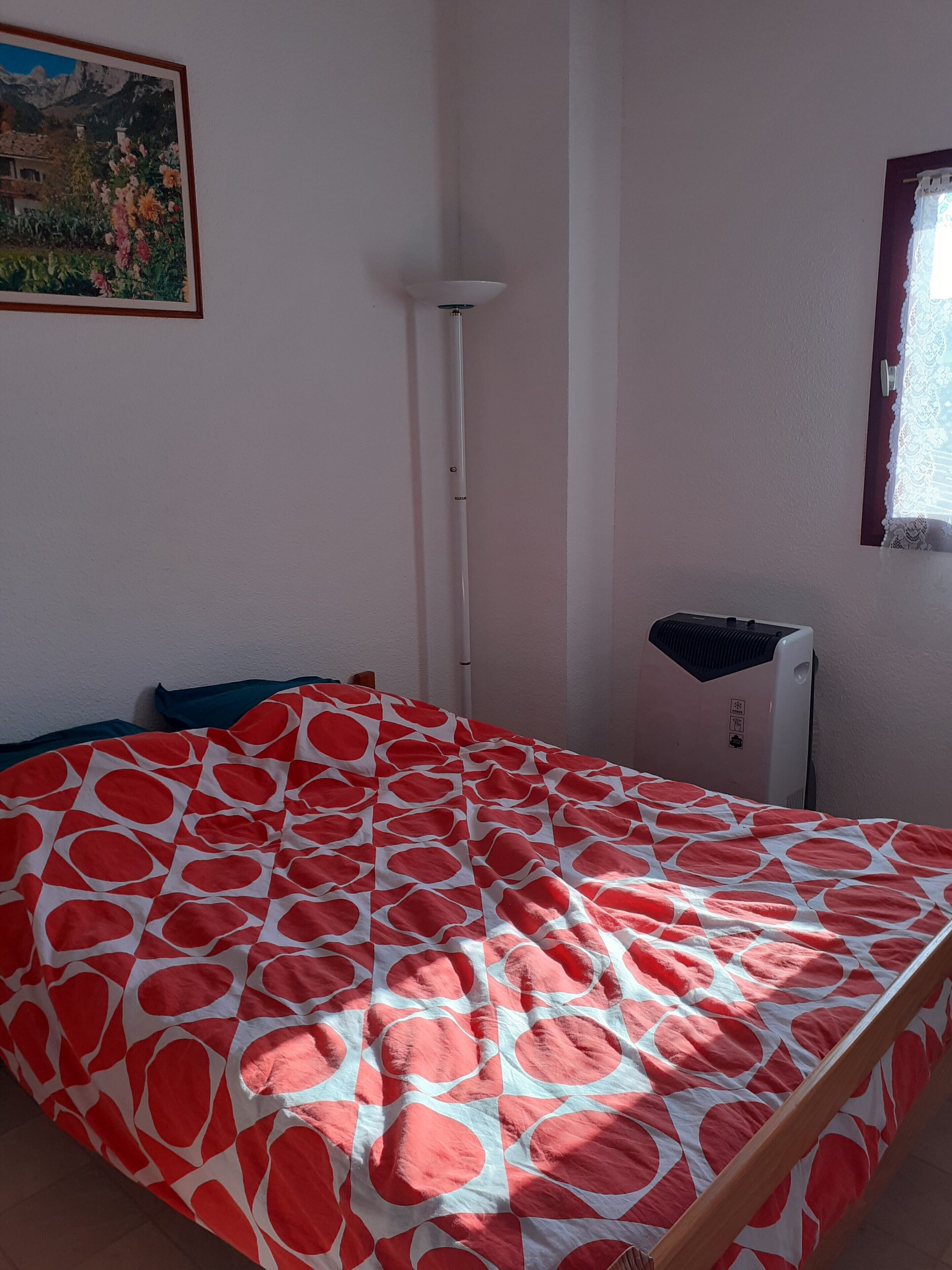 Une chambre à coucher avec un lit, une lampe sur pied, un radiateur et une fenêtre ornée de rideaux en dentelle.