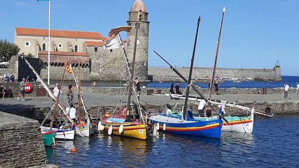 A harbor with several colorful boats docked, a stone building with a dome, and a clear blue sky.