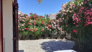 A courtyard with a stone floor, surrounded by flowering plants and a white table.