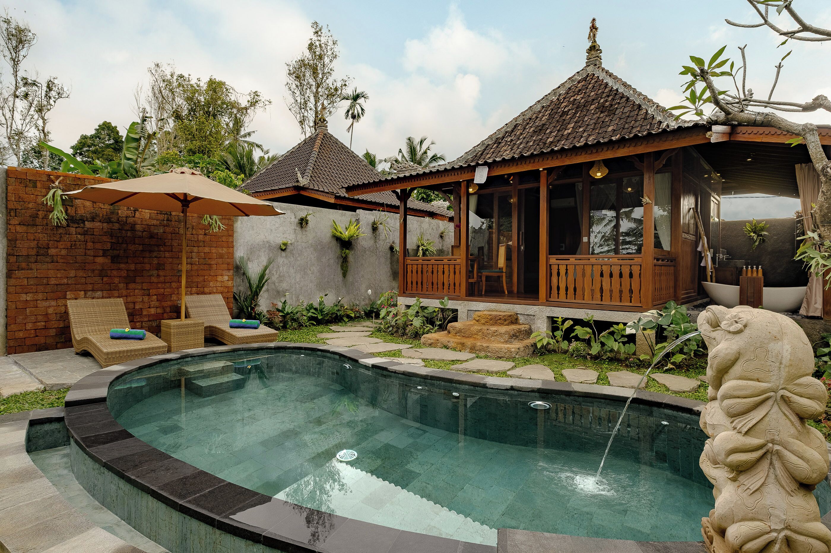 A swimming pool with a stone edge, a wooden deck with lounge chairs, and a covered seating area with a tiled roof.