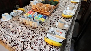 Ein Frühstückstisch ist gedeckt mit Brot, Früchten und Getränken, umgeben von Stühlen.