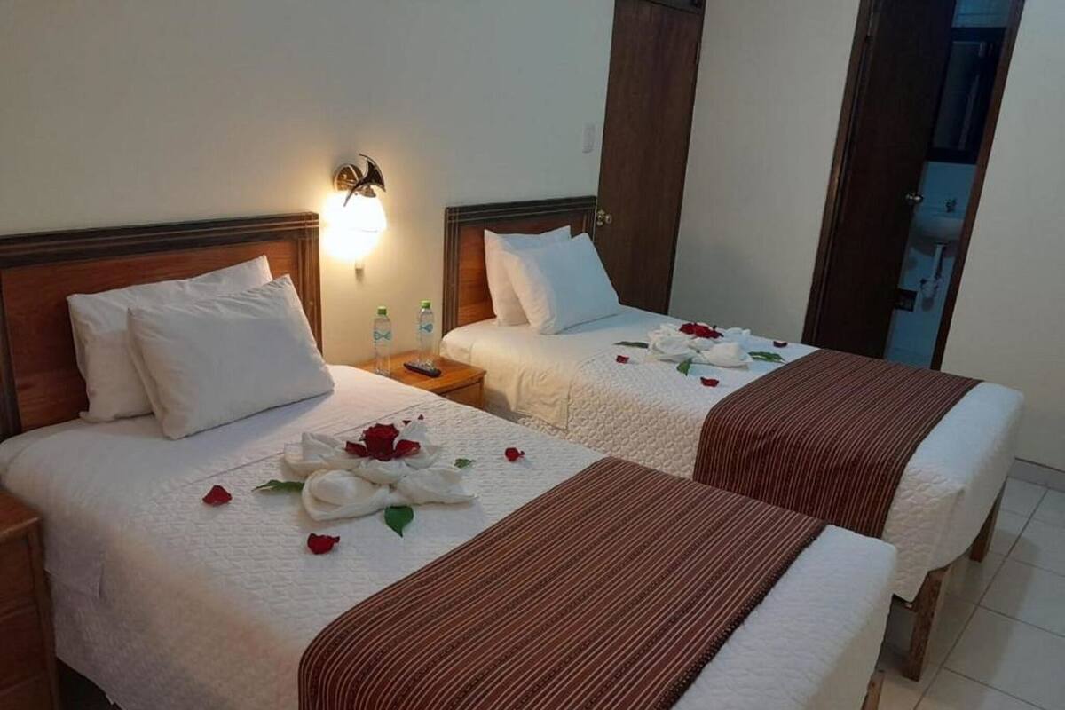 Dos camas con sábanas blancas, una mesita de noche con lámpara y una puerta de madera.