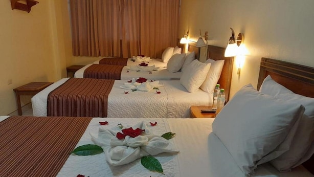 Ein Hotelzimmer mit zwei Betten, jeweils mit weißer Bettwäsche und dekorativen Blumenarrangements. Nachttischlampen und ein kleiner Tisch mit einer Fernbedienung sind vorhanden.