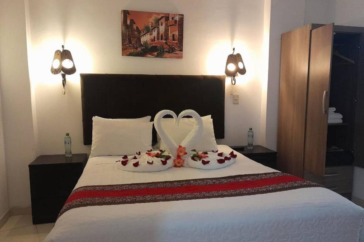 Habitación de hotel con una cama grande, dos mesitas de noche, un armario y un cuadro en la pared.