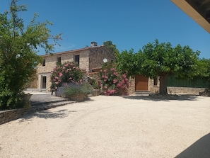 A stone building with a gravel driveway, surrounded by flowering plants and trees.