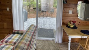 A cozy cabin interior with a wooden interior, a dining area with a table and chairs, and a sliding glass door leading to an outdoor patio.