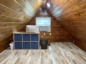 Cozy attic retreat with air conditioning, storage bench, and window with blinds.