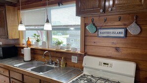 A kitchen with wooden cabinets, a stainless steel sink, a white stove, and a window with blinds.