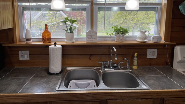 A kitchen with two sinks, wooden cabinets, a window with blinds, and hanging pendant lights.