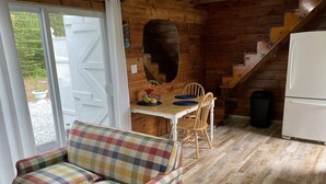 A cozy cabin interior with a plaid sofa, wooden dining table, chairs, a refrigerator, and a staircase.