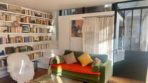 Una sala de estar acogedora con un sofá verde, una mesa de centro de vidrio y una estantería llena de libros.