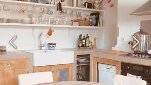 Una cocina compacta con armarios blancos, un fregadero y una estufa. Hay repisas sobre el fregadero con diversos utensilios de cocina y un jarrón con flores.