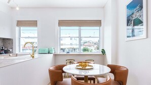 Una cucina moderna con una finestra, un'area pranzo con un tavolo rotondo e sedie, e vista sugli edifici esterni.