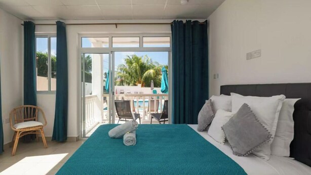 A hotel room with a bed, a chair, and a balcony with a view of palm trees. - Cap Confort (Mahé Island)