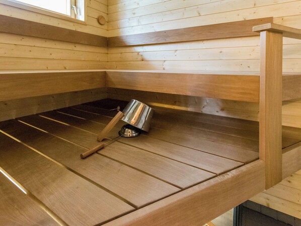 A sauna with wooden benches and a metal container, likely for water or steam. - Hiljanrinne by Interhome (Hausjärvi)