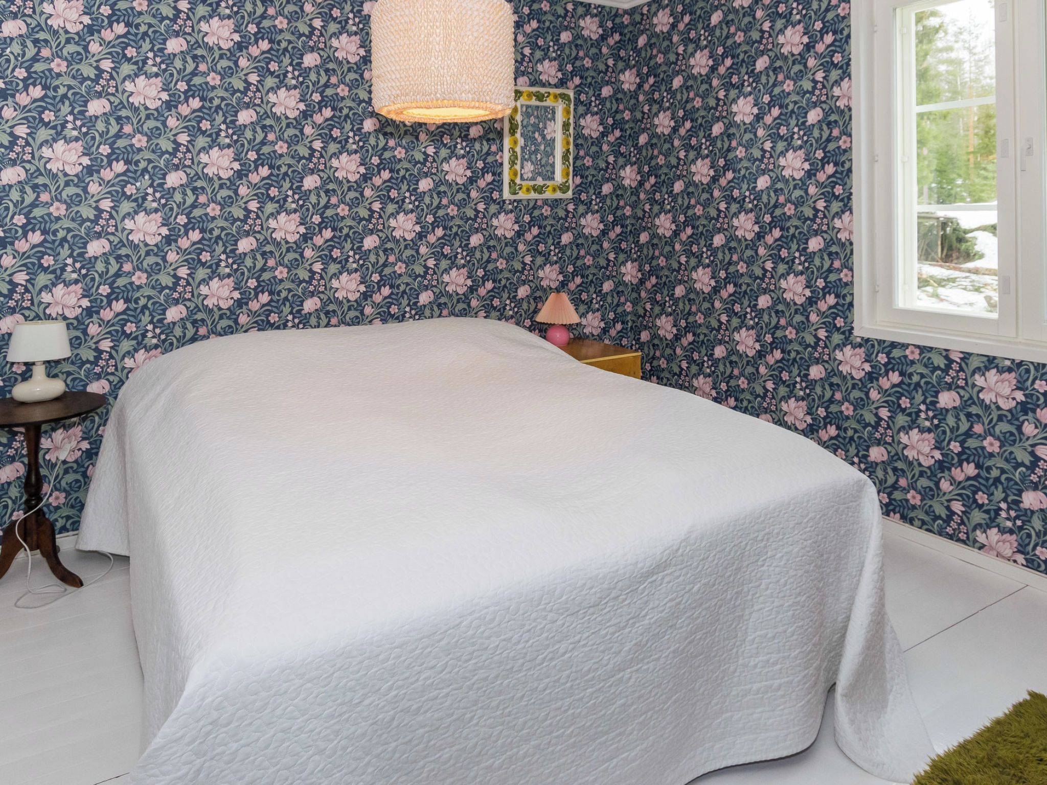 Ein Schlafzimmer mit einem Bett, einer Lampe, einem Bilderrahmen und einem Fenster.