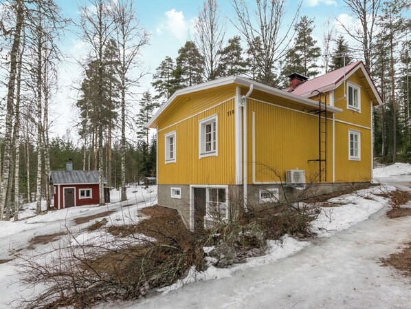 Une maison jaune à deux étages, avec un garage rouge, entourée d’un paysage enneigé et d’arbres.