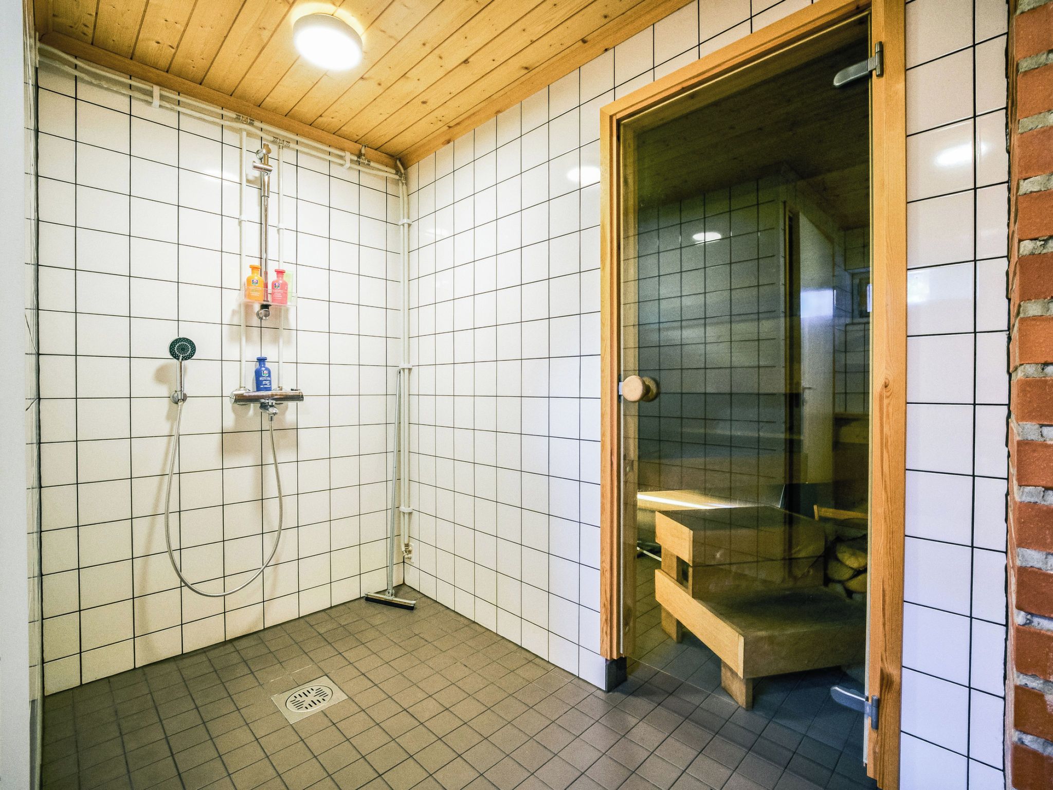 Et lille badeværelse med fliser, en bruseniche, toilet og en bænk.