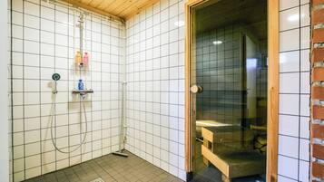 Et lille badeværelse med fliser, en bruseniche, toilet og en bænk.