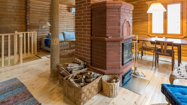 Ein gemütliches Blockhaus-Interieur mit Kamin aus Backsteinen, Holzdielen, einem Essbereich und einem Lager für Brennholz.
