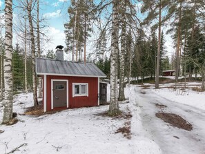Une petite cabane avec un toit en métal, entourée de grands arbres et d’un sol recouvert de neige.
