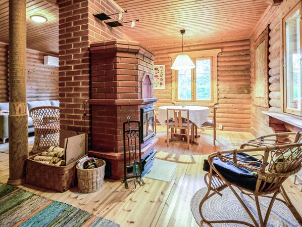 A cozy log cabin interior with a fireplace, wicker furniture, and a dining area.