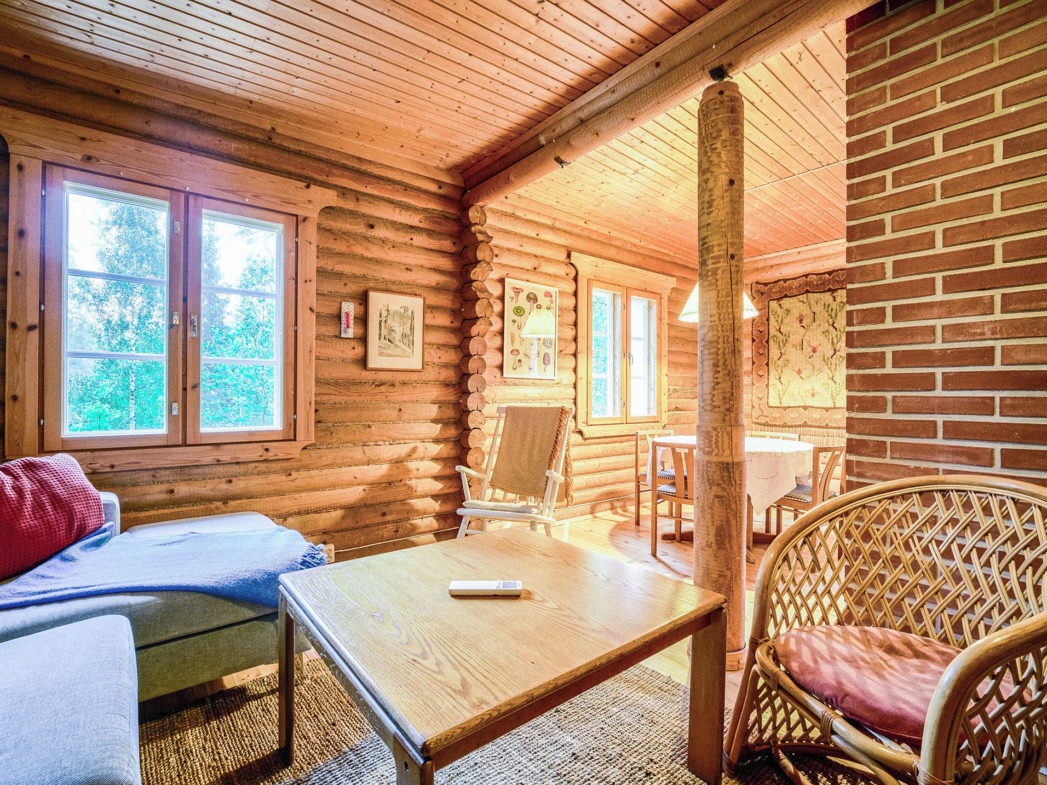 L’intérieur d’une cabane en rondins, avec un lit, une table, une chaise en osier et un coin repas.