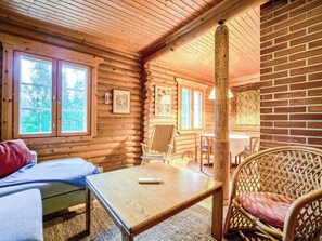 Ein rustikales Blockhaus-Interieur mit einem Bett, einem Tisch, einem Korbstuhl und einem Essbereich.