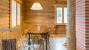 Ein Holzblockhaus-Interieur mit einem Holzesstisch, Stühlen und einer Bank mit Kissen.