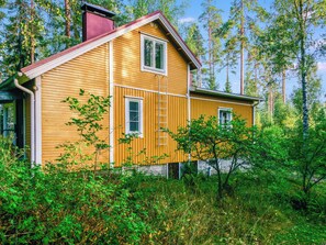 Une maison en bois avec un toit rouge, entourée d’une végétation luxuriante et de grands arbres.